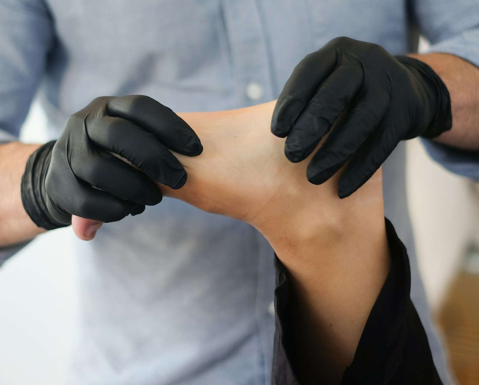 Manos con guantes de un fisioterapeuta trabajando el pie y el tobillo de un paciente